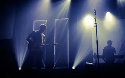Anonymous male musician performing melody with guitar on stage near microphone and DJ in dark club with spotlights