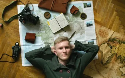 Young man dreams of travel, surrounded by maps, camera, and notebook.