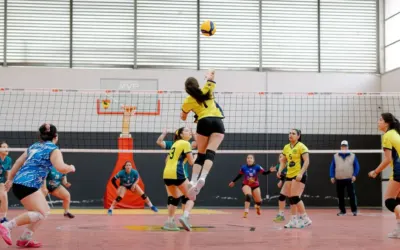 Dynamic shot of a volleyball player jumping for a spike in an indoor game. Vibrant team uniforms add energy.